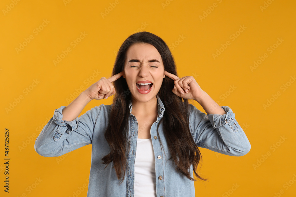 Emotional young woman covering ears with fingers on yellow background Emotional young woman covering ears with fingers on yellow background