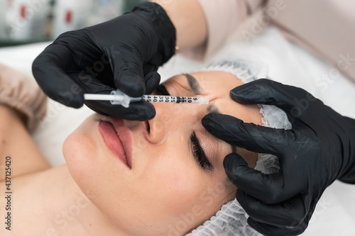 Cosmetologist doctor gives botox injection in the eyebrow or forehead. Young woman gets beauty facial injections. Face rejuvenation and hydration procedures. Aesthetic face cosmetology