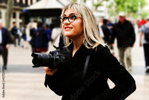 Young blonde woman, with glasses and camera in the hand, looking away.
