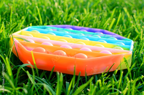Trendy silicone colorful rainbow antistress pop it toy for baby on green grass. Top view.