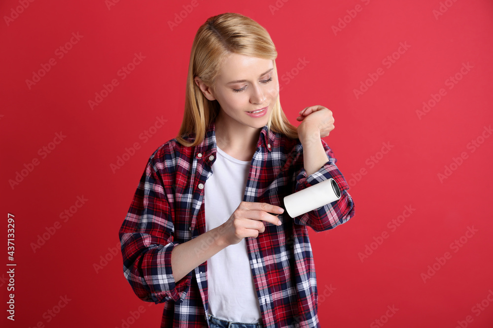 Young woman cleaning clothes with lint roller on red background Young woman cleaning clothes with lint roller on red background