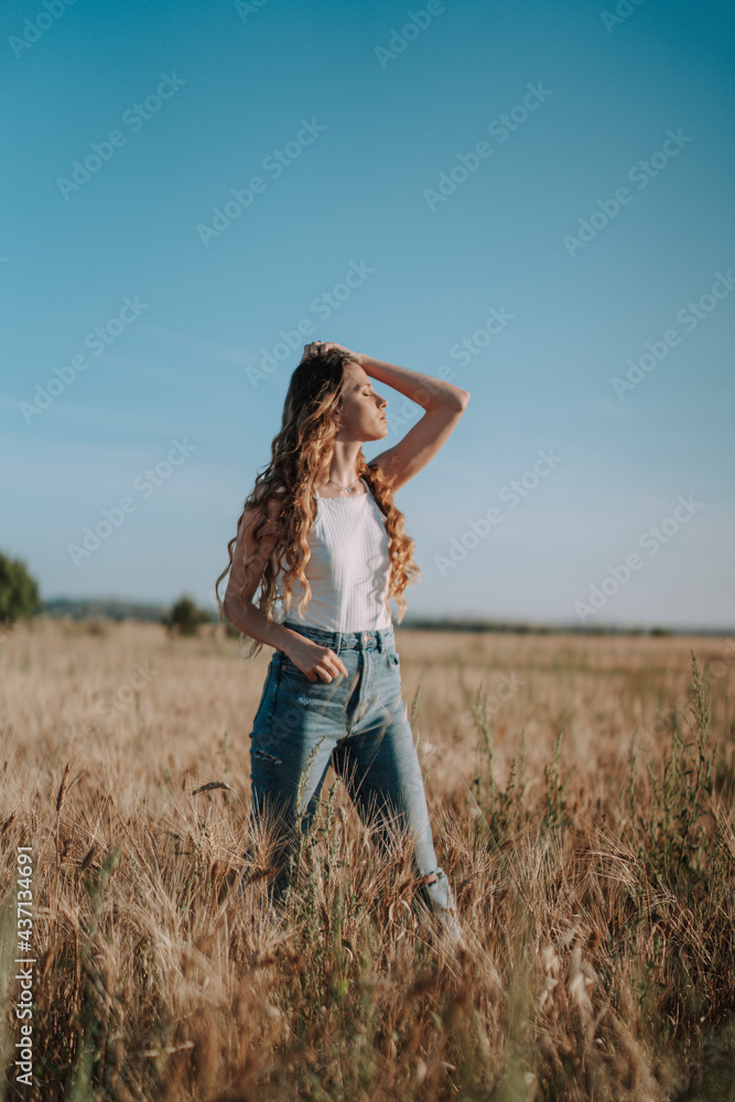 Chica joven atractiva posando en mitad de un campo de trigo al atardecer con tonos dorados Chica joven atractiva posando en mitad de un campo de trigo al atardecer con tonos dorados