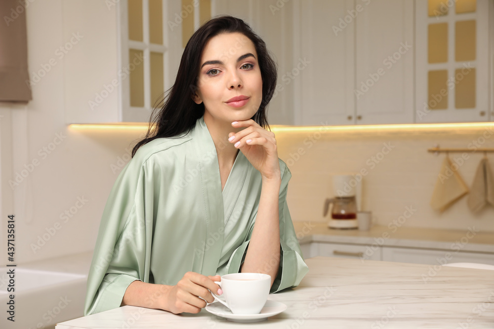 Pretty young woman wearing beautiful silk robe with cup of coffee in kitchen. Space for text Pretty young woman wearing beautiful silk robe with cup of coffee in kitchen. Space for text
