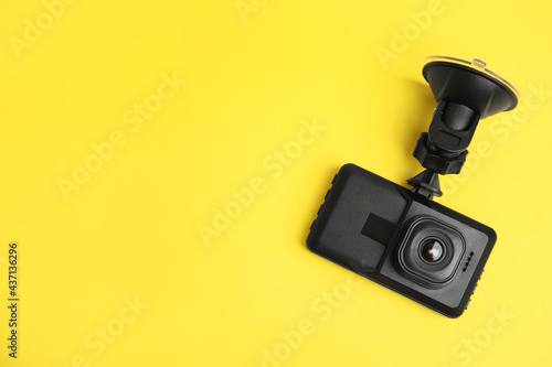 Modern car dashboard camera with suction mount on yellow background, top view. Space for text photo