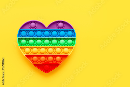 Colorful trendy Pop it fidgets heart shape toy on a bright yellow background. Toy anti-stress, simple dimple. LGBT concept photo