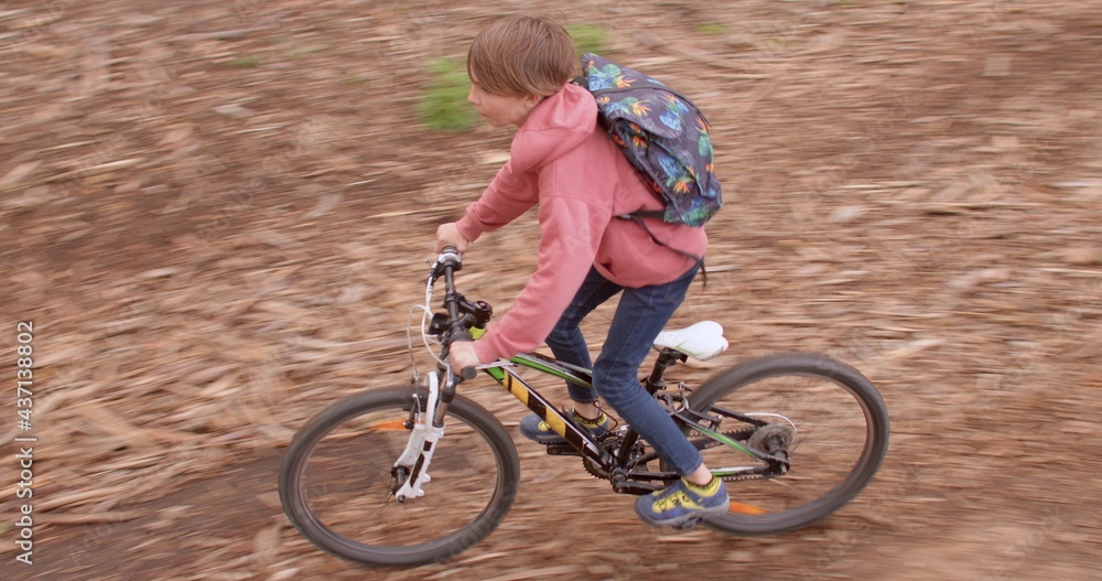 Fototapeta premium A teenager rides a bicycle in the woods. He rolls down a hill along a forest road. Weekend travel. Active lifestyle. Camera movement.