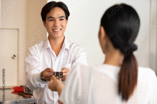 male receptionist or hotel front desk smiling and receiving credit card from woman guest