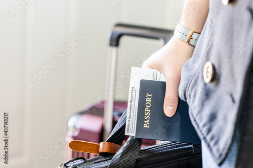 Hand holding passport and approved vaccination record card with laptop bag for business trip. Citizen identity and vaccinated documents of passenger require for travel during pandemic in new normal.