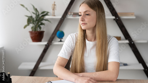 Portrait of attractive blonde young woman 20s with long hair bored student unmotivated sitting at the table studying at home. Work tired and sad.