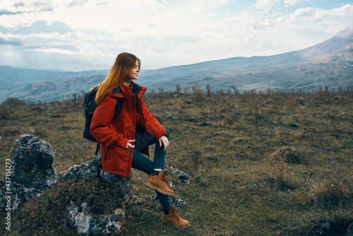 woman traveler in a jacket sits on the Big Stone and looks at the mountains landscape
