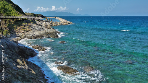A pedestrian path with a rope railing winds along the mountainside, above the sea. Turquoise waves foam on the stones. Summer sunny day. Vietnam. Nha Trang