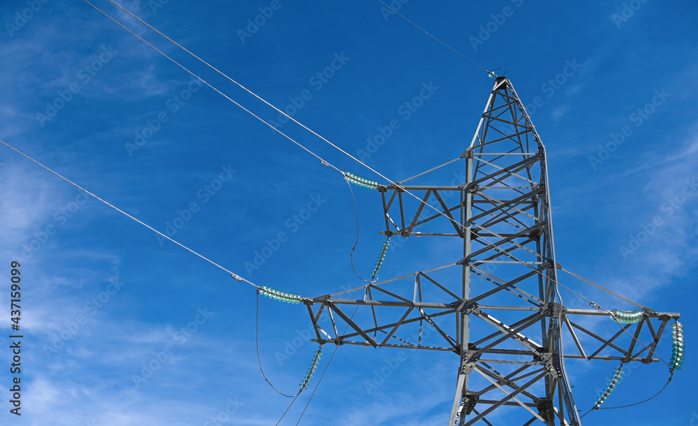 High voltage power tower with glass insulators, against a blue sky with ...
