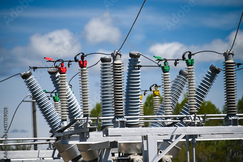 High voltage ceramic insulators on a transformer, against a blue sky with white clouds.