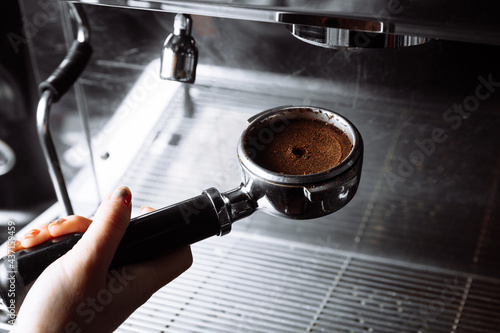 Barista pressing ground coffee into portafilter by tamper.