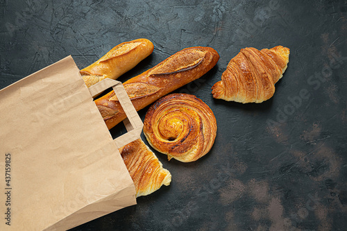 French snail bun, croissants and baguette in an eco-friendly paper bag on a dark background, zero waste concept, top view photo