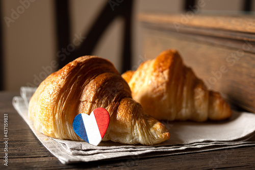 Two fresh french croissants and a heart in the colors of the French flag on a table