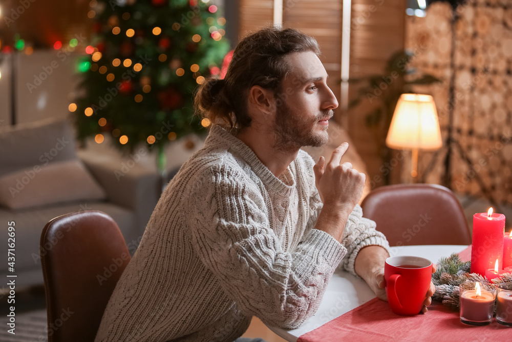 Handsome man sitting at table in room decorated for Christmas Handsome man sitting at table in room decorated for Christmas