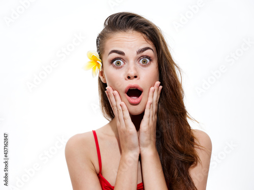 woman with open mouth touching face with hands and yellow flower in hair