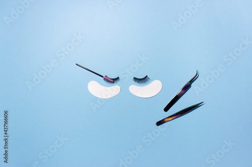 Artificial eyelashes, patches and tweezers on a blue background, top view. The concept of the lashmaker, artificial eyelash extension.
