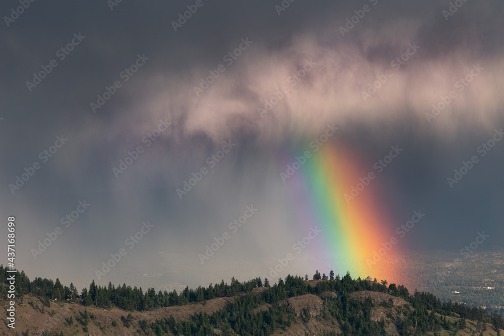 View of Kelowna during rain.  Rainbow.  Rainbow on the background of dark clouds over the hill.  Rainbow over Knox Mountain Park in Kelowna, Okanagan, British Columbia, Canada.