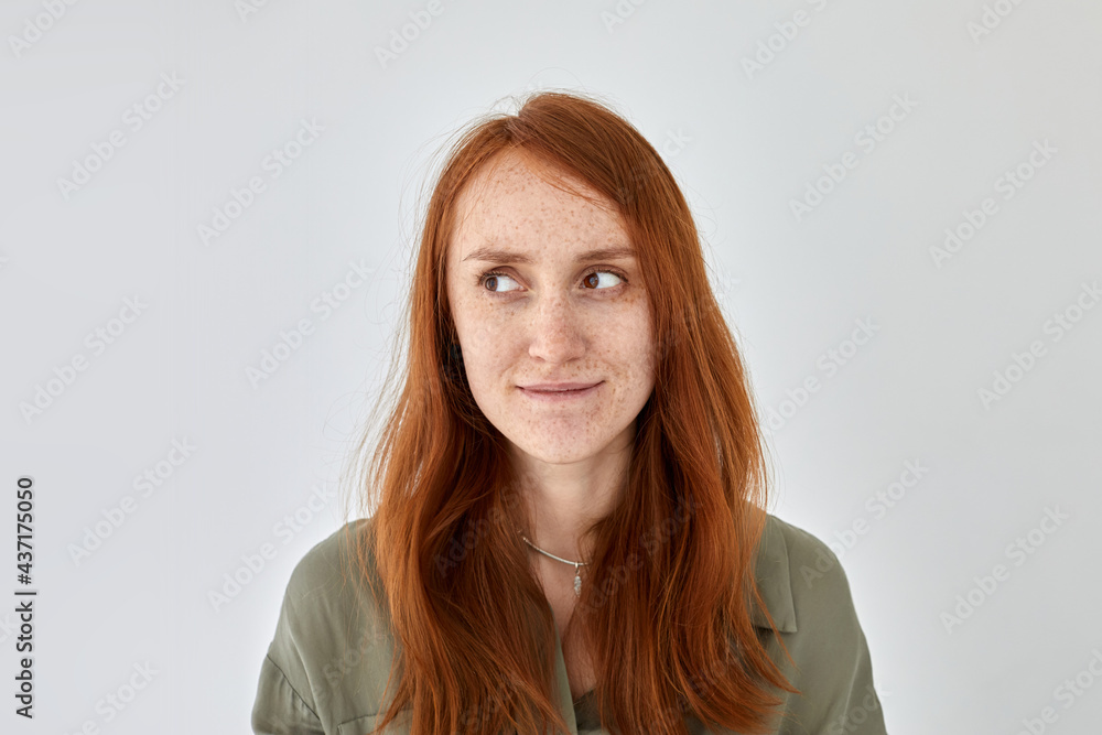 Obraz premium Portrait of glad female with ginger hair and freckles standing on white background and looking away