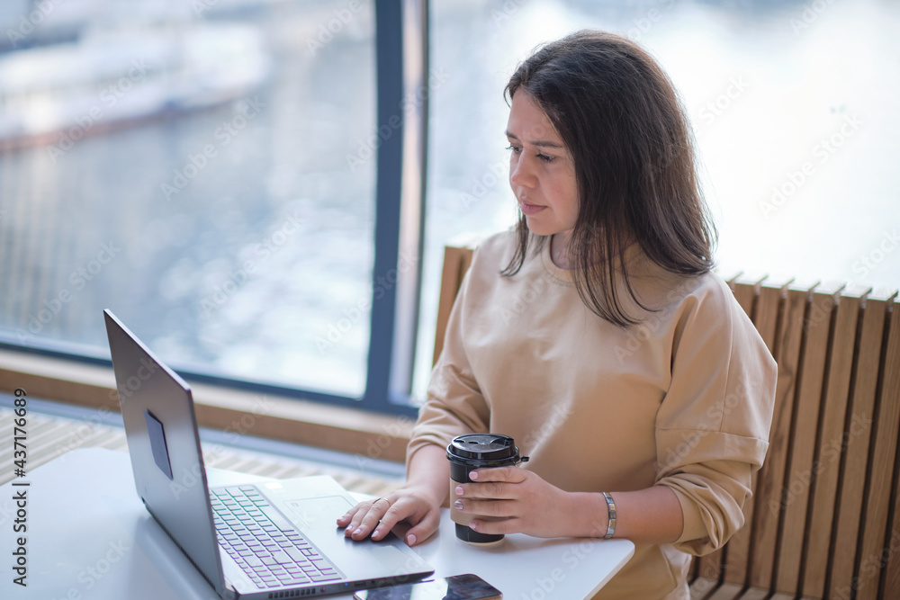 happy woman using laptop while sitting at cafe. Girl browsing internet, chatting, blogging. Brunette studying on laptop and enjoying coffee happy woman using laptop while sitting at cafe. Girl browsing internet, chatting, blogging. Brunette studying on laptop and enjoying coffee