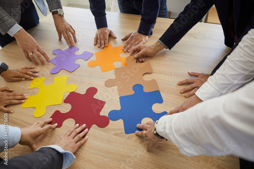Creative group looking for a professional business solution. Team of people standing around an office table trying to match colorful jigsaw puzzle pieces as a metaphor for teamwork and problem solving