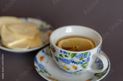 Cup of tea with lemon and Saucer with sliced cheese on gray background.