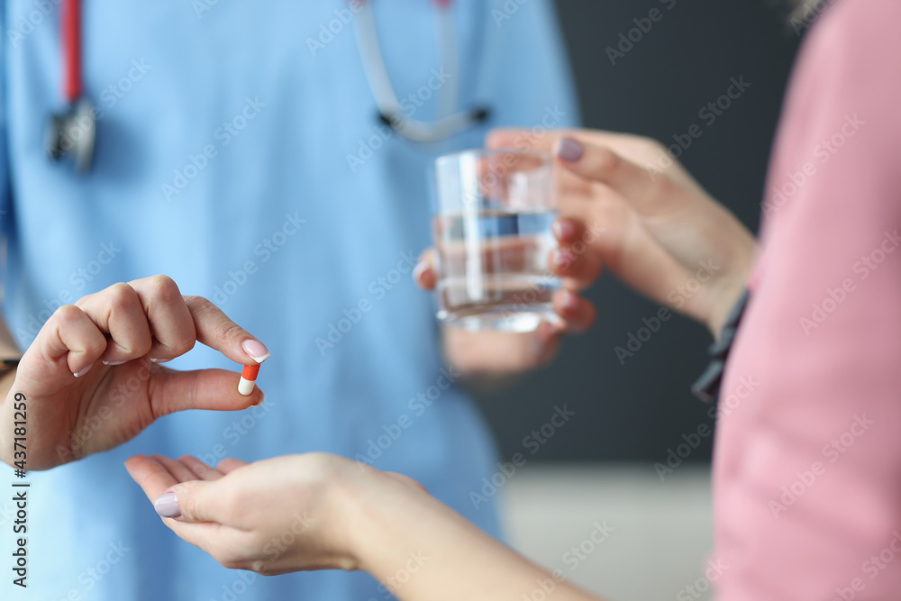 Doctor giving patient glass of water and capsule of medicine in clinic closeup Doctor giving patient glass of water and capsule of medicine in clinic closeup