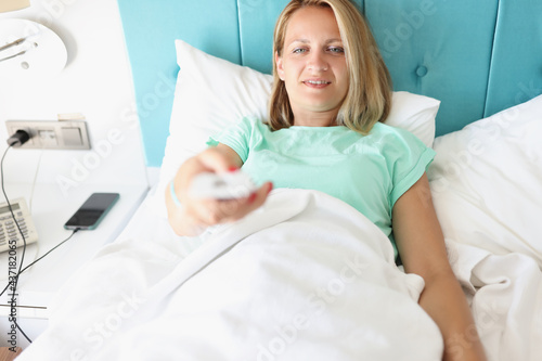 Young woman lying in bed with TV remote control in her hands