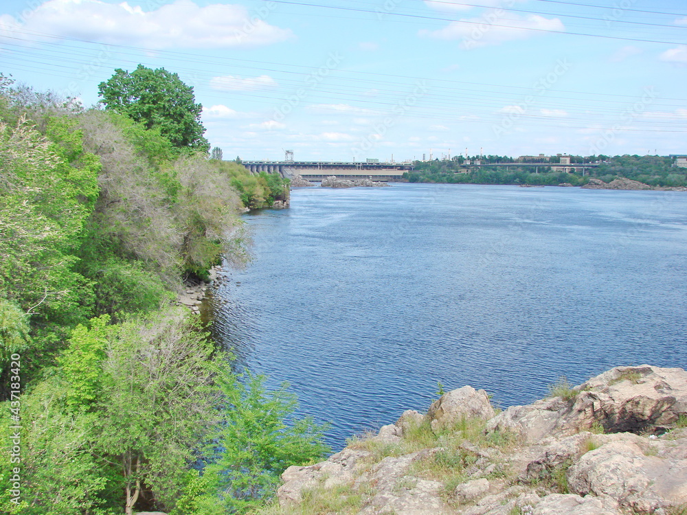 Walk on a narrow path on top of the Dnieper bank on the background of a dam under white clouds on the horizon.