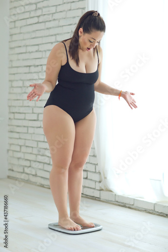 A fat woman weighs herself in and cannot wear good clothes. High quality photo.