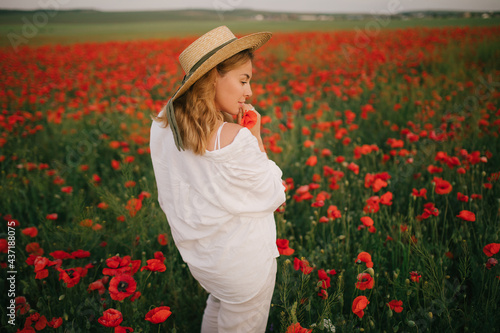 Young beautiful woman wearing white linen suit and straw hat posing in a poppy field. © polinaloves