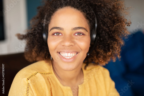 Close-up portrait of cheerful optimistic dark-skinned young woman with curly Afro hairstyle wearing headset, natural beauty mixed-race female employee in headphones with a mic looks at the camera