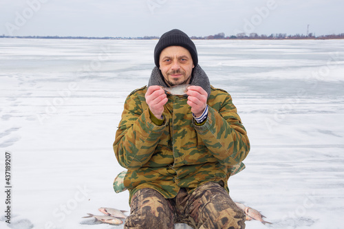 A 40-year-old European man is engaged in winter fishing. The fisherman holds a small fish in his hands.