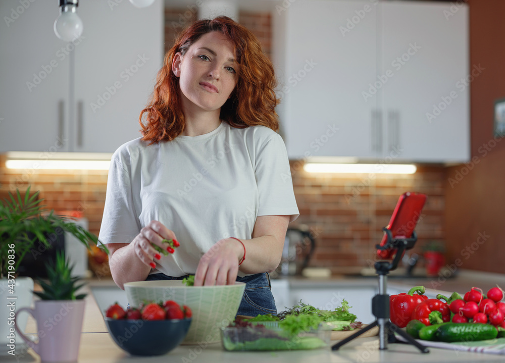 Young pretty woman blogger shoots a video of a salad recipe on a smartphone camera.