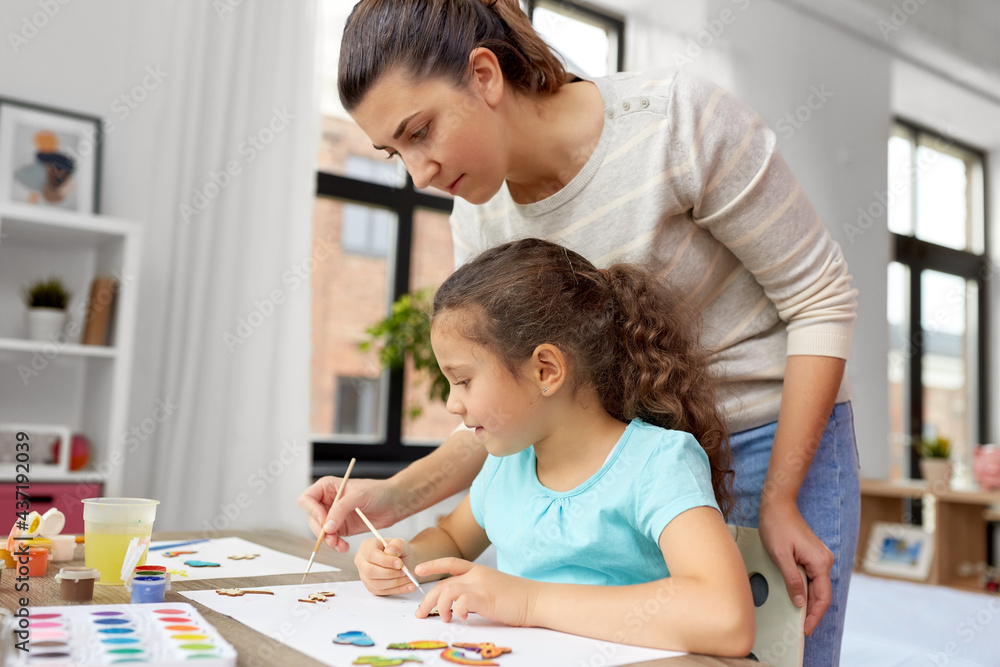 family, motherhood and leisure concept - mother spending time with her little daughter drawing or painting wooden chipboard items with colors at home family, motherhood and leisure concept - mother spending time with her little daughter drawing or painting wooden chipboard items with colors at home