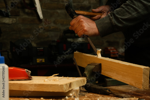 Carpenter chiselling wooden plank in the workshop.