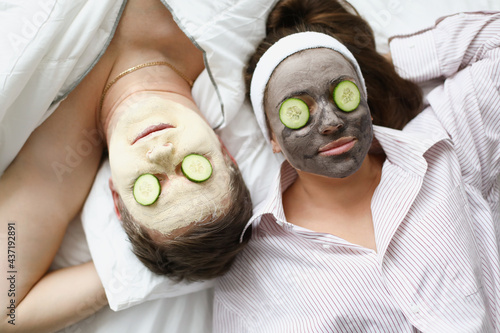Man and woman apply clay mask for rejuvenation on face and cucumbers on eyes