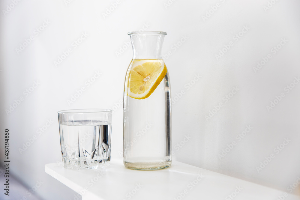 A refreshing glass of water, a bottle with a slice of lemon inside is on the dresser in summer heat A refreshing glass of water, a bottle with a slice of lemon inside is on the dresser in summer heat