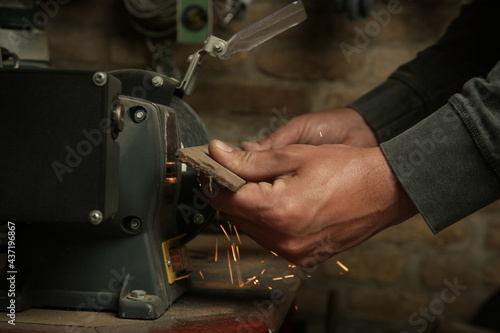Handyman sharpening iron tool on electrical grinder stone