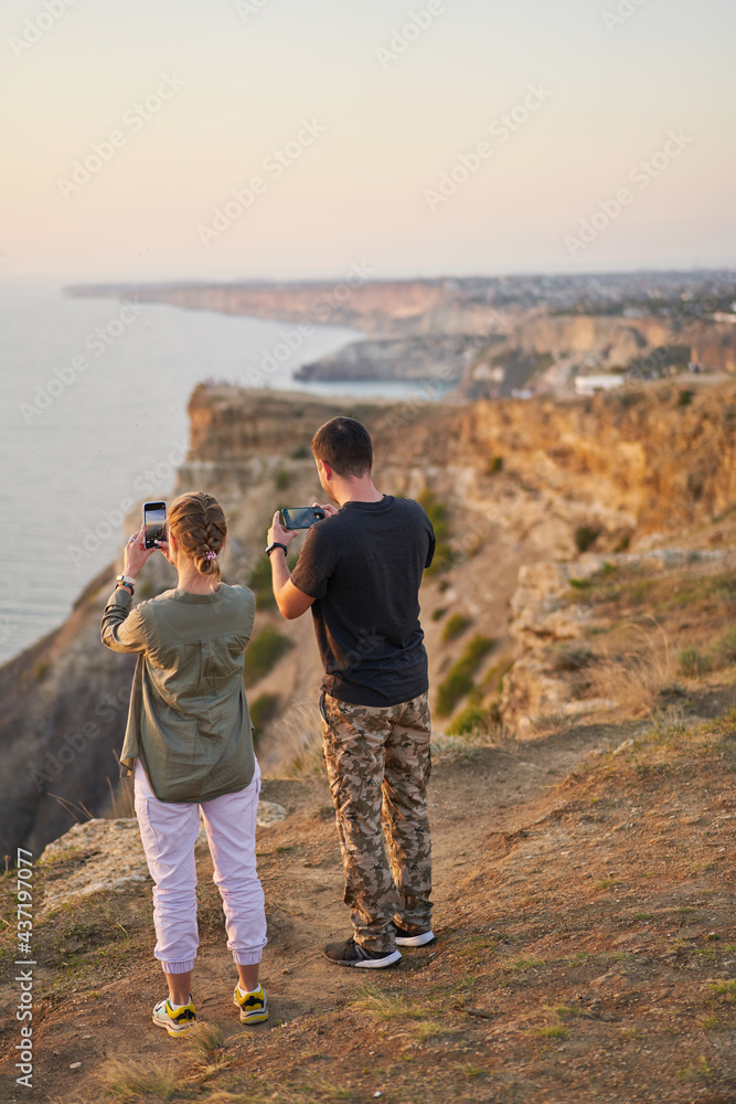 Couple is staying on the rock, taking photo and enjoying the sea view and the fresh air.