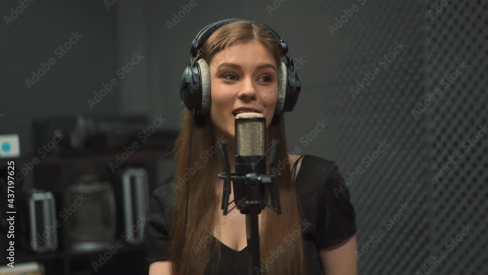 Happy long haired young lady performer with large headphones records new song with contemporary microphone dancing in audio studio close view Happy long haired young lady performer with large headphones records new song with contemporary microphone dancing in audio studio close view