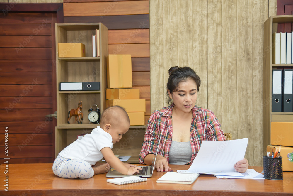 Pretty young single mom working at home, holding the document while little daughter playing a laptop on desk. Pretty young single mom working at home, holding the document while little daughter playing a laptop on desk.