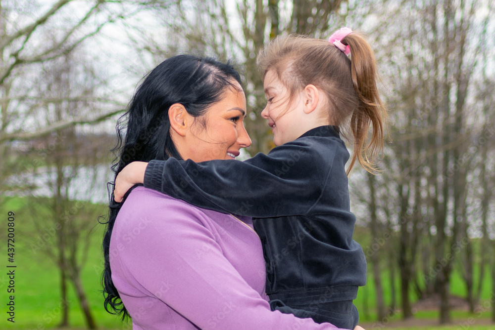 Beautiful mother and daughter play hugs in a spring park nature in profile looking at each other.