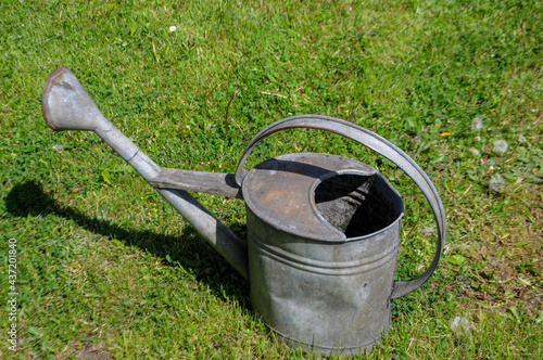 Metal old-fashioned watering can on the green grass in the garden