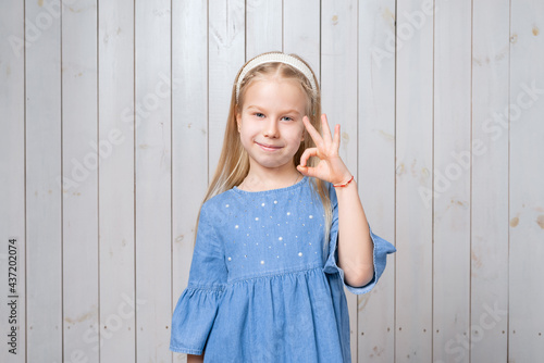 Portrait of attractive little girl in blue dress showing OK gesture with hand