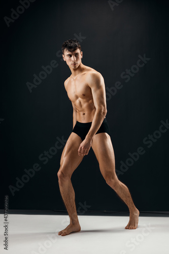 man with muscular naked body in black panties on a dark background