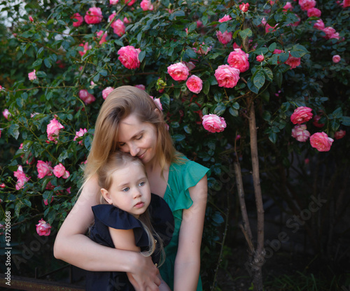 mom hugs her little daughter against the background of a rose bush