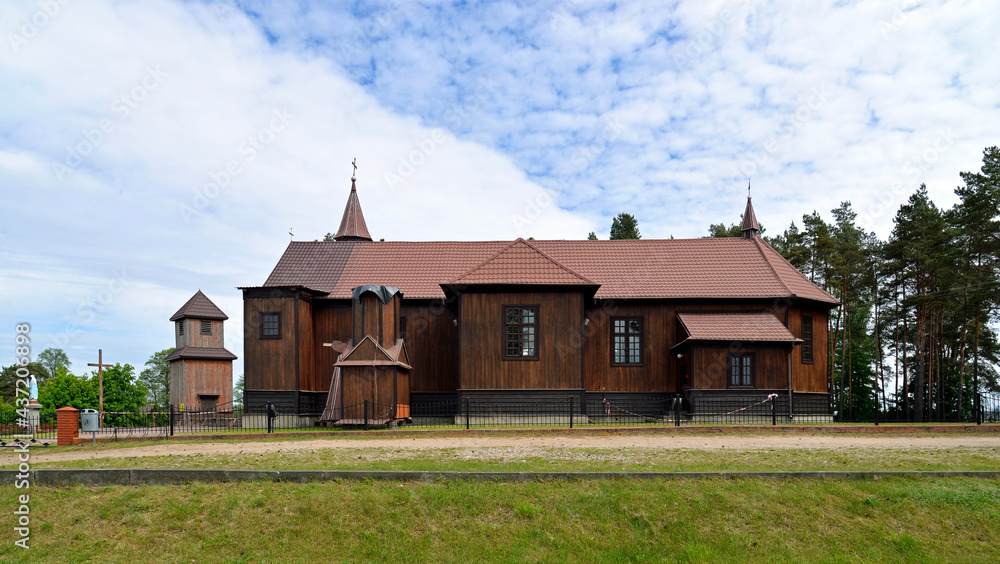 Obraz premium Built in 1925, a historic wooden Catholic church dedicated to Saint Roch in the village of Leman in Podlasie, Poland. There is also a historic wooden belfry next to the church.
